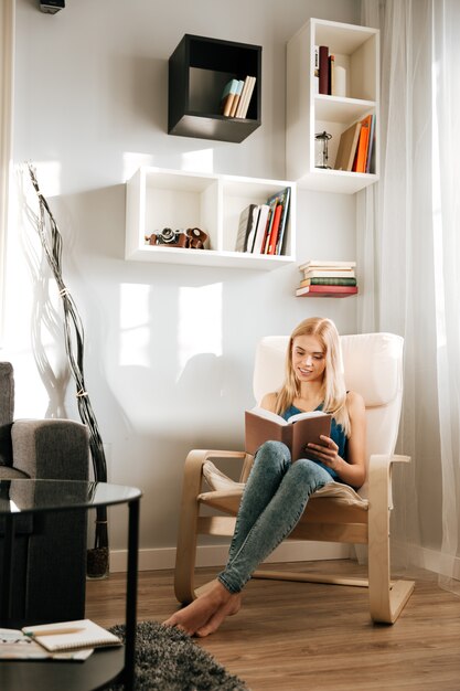 Smiling woman sitting in chair and reading book at home