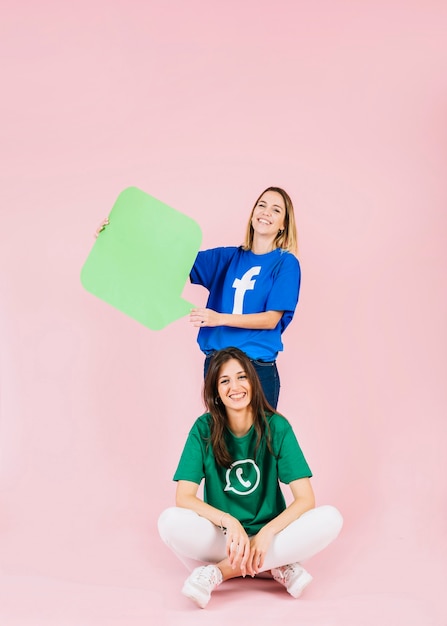 Free photo smiling woman sitting in front of her friend holding green speech bubble