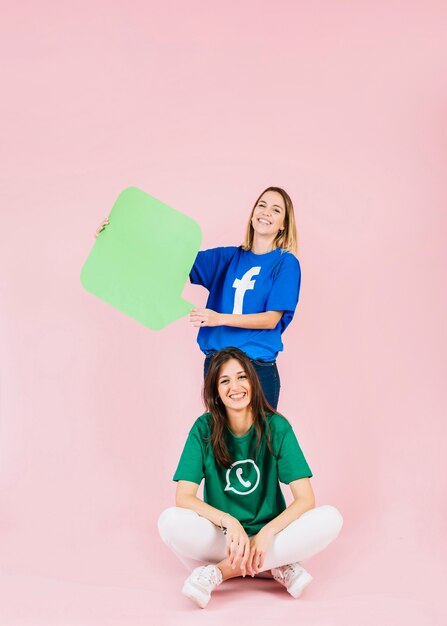 Smiling woman sitting in front of her friend holding green speech bubble