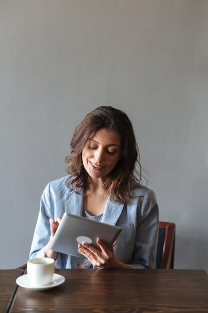 Smiling woman sitting indoors using tablet computer.