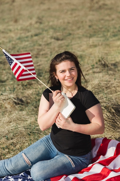 Smiling woman sitting on stripe banner and holding American flag 