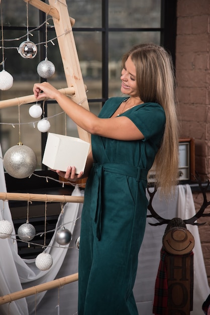 Smiling woman standing with a Christmas present at home and hanging a toy