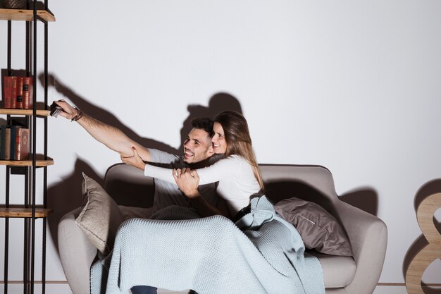 Smiling woman stopping man to put TV remote on shelf on sofa