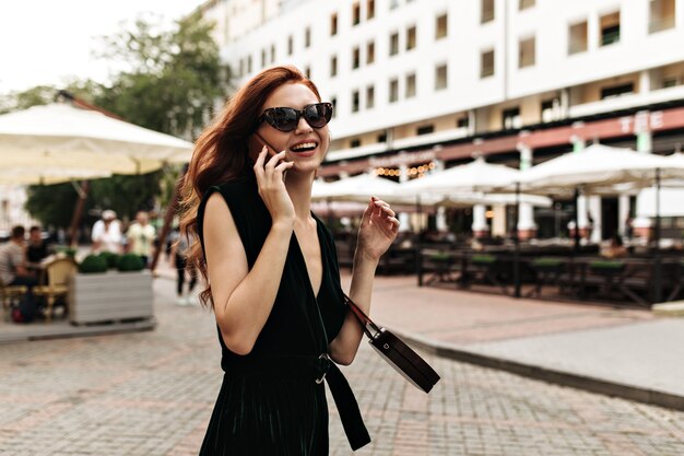 Smiling woman in sunglasses and dress talks on phone