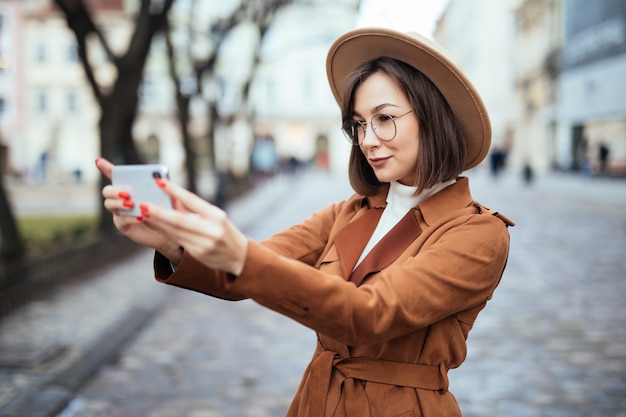 秋の日の外で彼女の電話で写真を撮って笑顔の女性