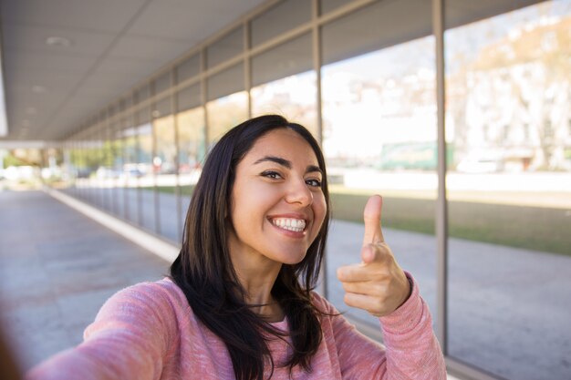 Selfie写真を撮るとあなたを屋外で指している笑顔の女性
