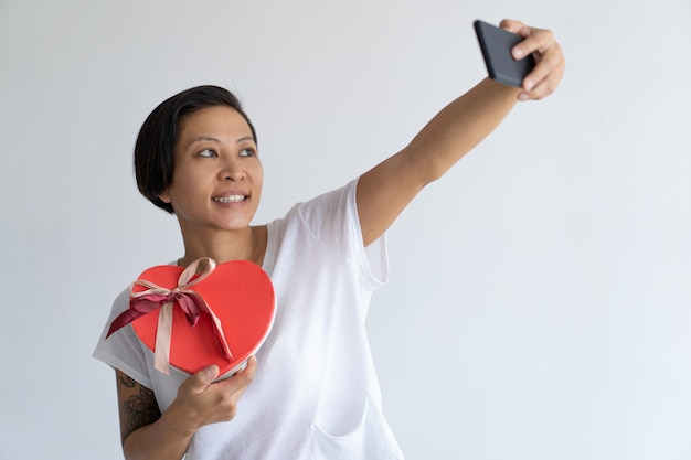 ハート型のギフトボックスとselfie写真を撮る笑顔の女性