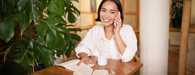 携帯電話の応答電話で話し、カフェに座って幸せそうに見える笑顔の女性