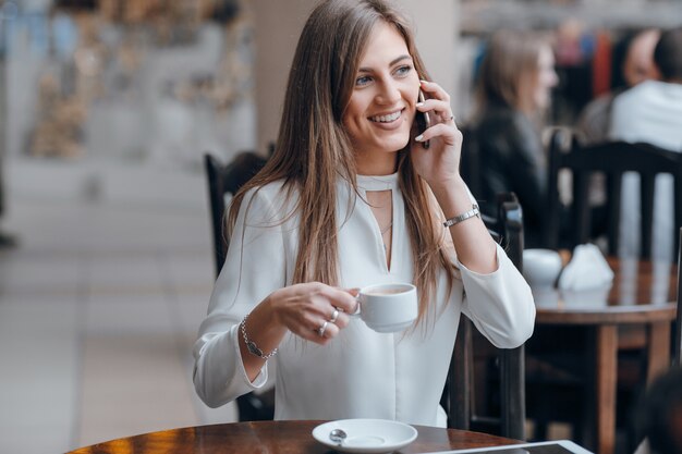 Smiling woman talking on the phone and holding a cup of coffee