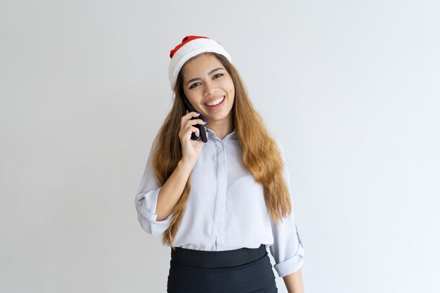 Smiling woman talking on smartphone and wearing Santa Claus hat