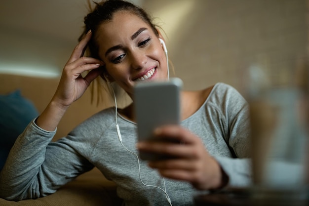 Улыбающаяся женщина пользуется мобильным телефоном и читает текстовое сообщение, отдыхая дома