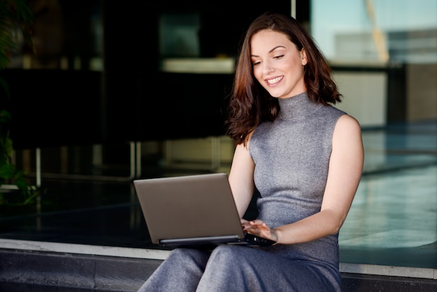 Free photo smiling woman using her laptop sitting in a modern place