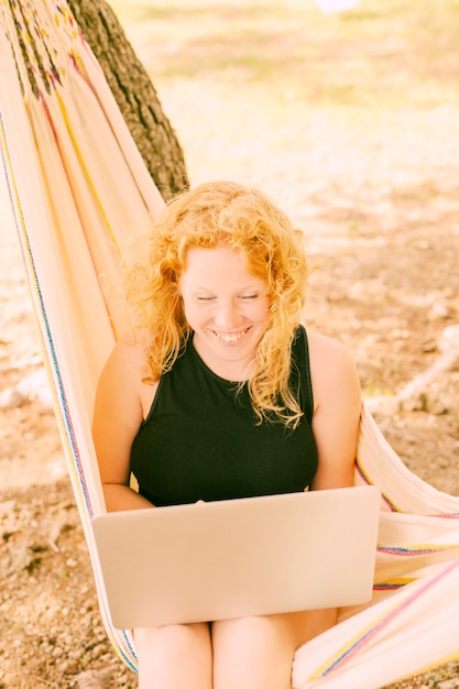 Donna sorridente che utilizza computer portatile nell'amaca