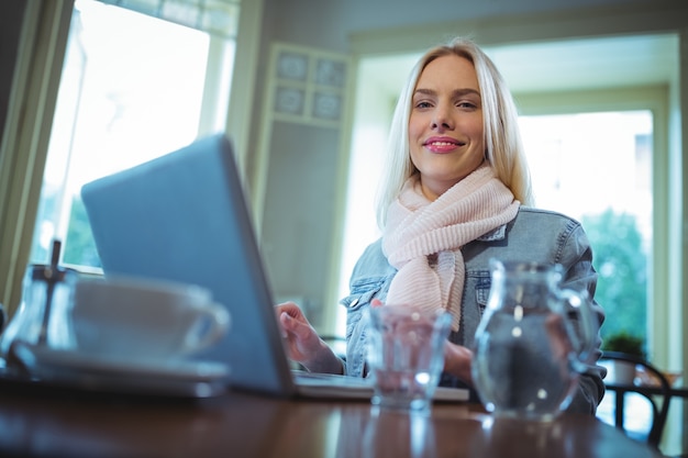 コーヒーを持ちながら、ラップトップを使用して女性を笑顔