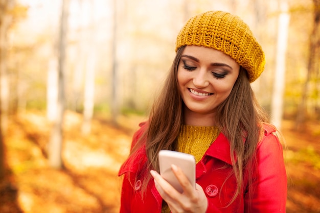 Улыбающаяся женщина с помощью мобильного телефона в парке осенью