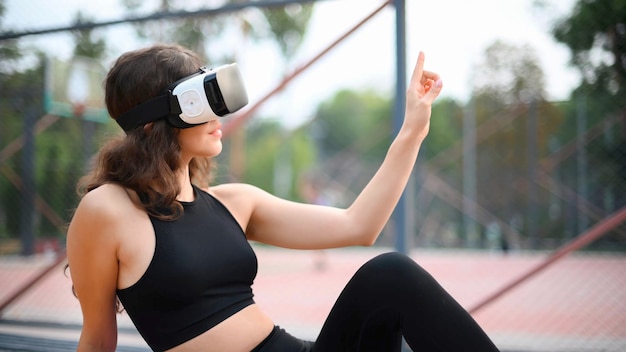 Foto gratuita donna sorridente che utilizza l'auricolare vr in una tuta da ginnastica mentre è seduto su un tappetino da yoga su un campo sportivo in un parco