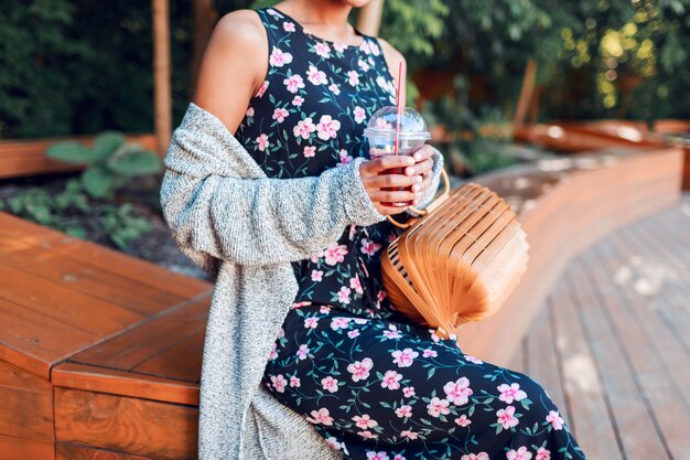 Smiling woman walking in sunny park and drinking lemonade