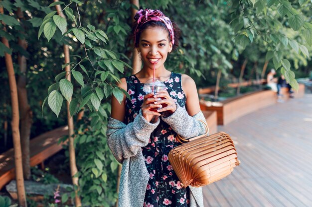 Smiling woman walking in sunny park and drinking lemonade