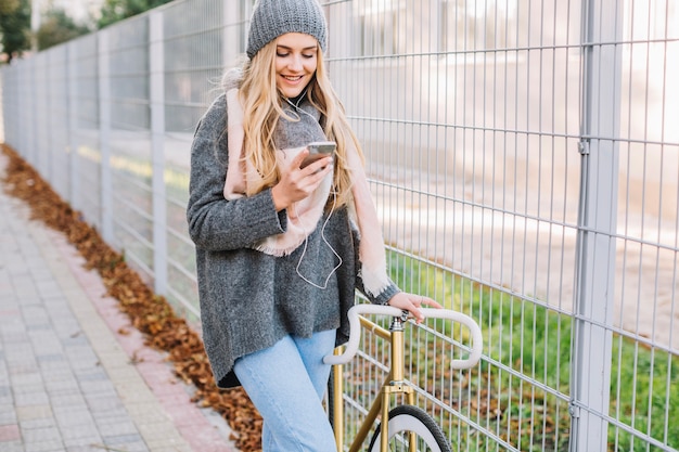 Smiling woman walking with smartphone and bicycle