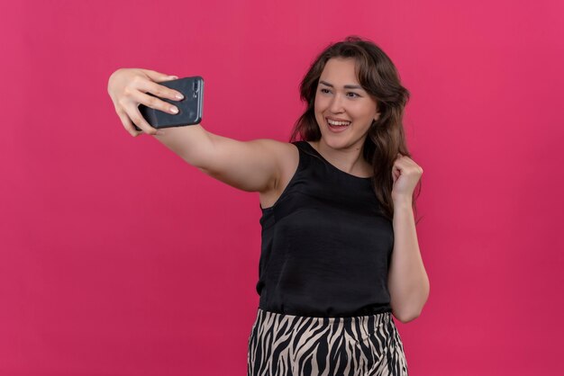 Smiling woman wearing black undershirt take a selfie on pink wall