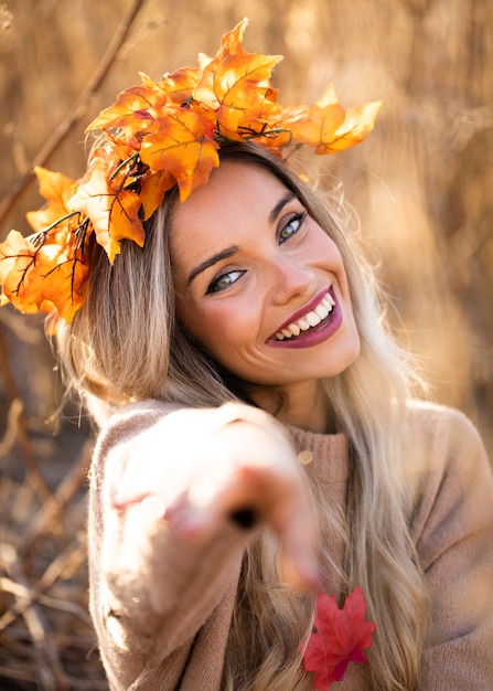 Smiling woman wearing dry maple leaves tiara pointing towards the camera