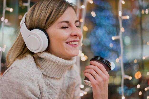 Smiling woman wearing headphones holding cup christmas lights