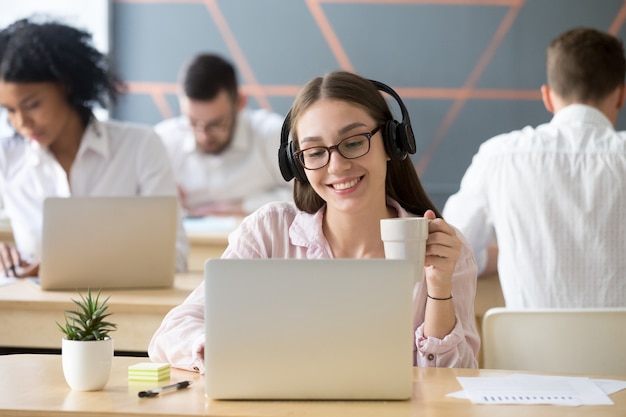 Smiling woman wearing headphones watching online video during coffee break