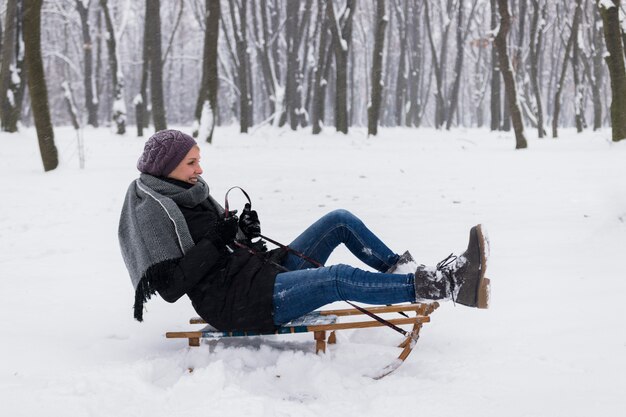 雪の風景をそりに座って暖かい服を着て笑顔の女性