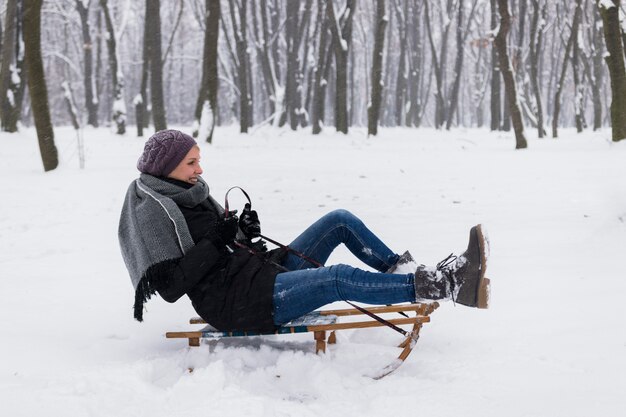 Улыбающаяся женщина в теплой одежде сидит на санях над снежным пейзажем