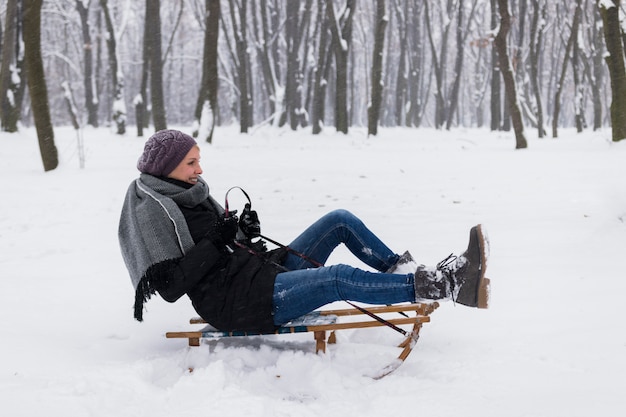 Smiling woman wearing a warm clothes sitting on sledge over the snowy landscape