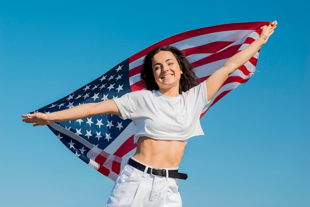 大きな米国旗を保持している白い服を着て笑顔の女性