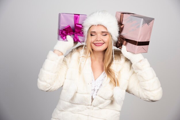 Smiling woman in winter outfit holding gift boxes.