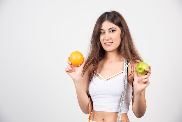 A smiling woman with an apple and an orange . 