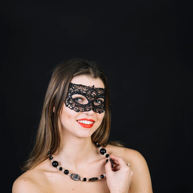 仮面舞踏会のカーニバルマスクを身に着けているビーズのネックレスを持つ女性の笑みを浮かべてください。