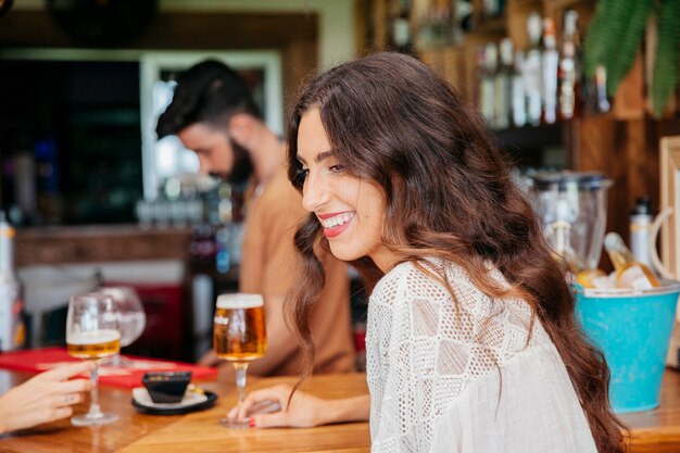 Smiling woman with beer sitting in bar