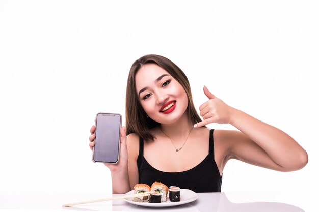 Улыбающаяся женщина с черными волосами и красными губами пробует роллы суши с деревянными палочками в руке и разговаривает по телефону