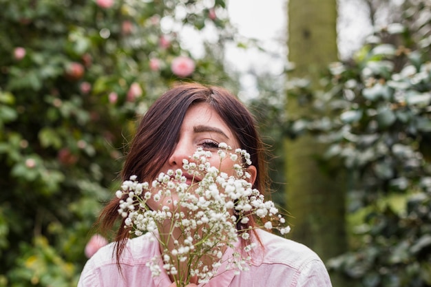無料写真 茂みに成長しているピンクの花の近くの植物の束を持つ女性の笑みを浮かべてください。