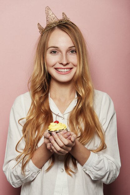 Smiling woman, with a crown, holding a birthday cupcake