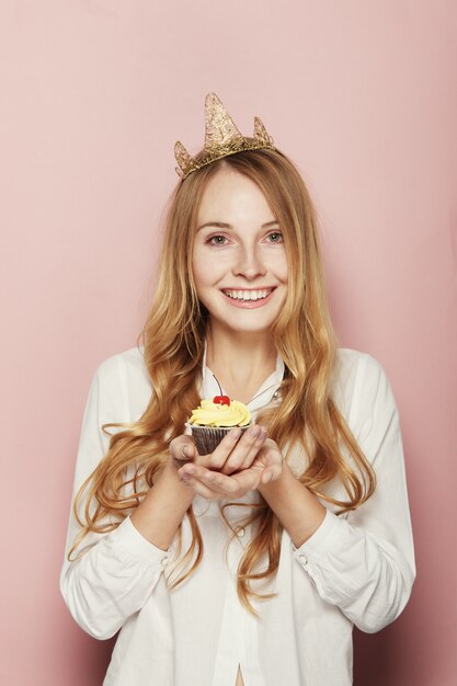 Smiling woman, with a crown, holding a birthday cupcake