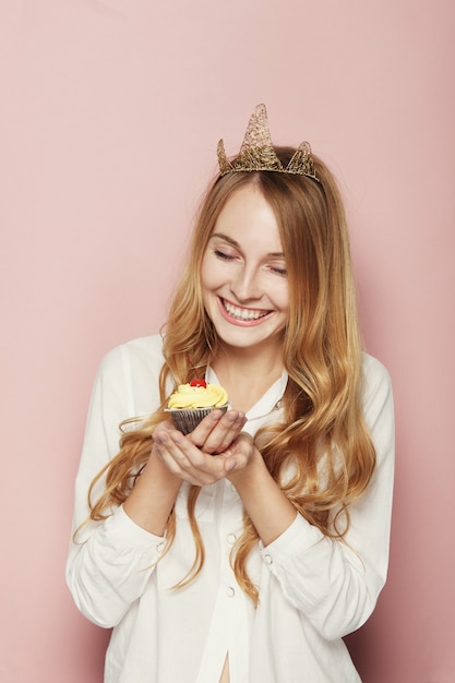 Smiling woman, with a crown, holding a birthday cupcake