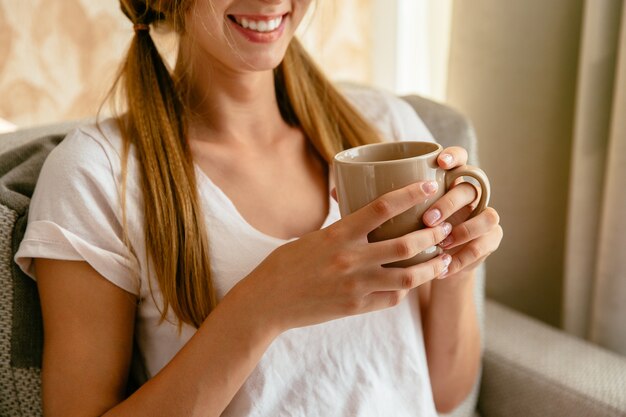 家庭で手に茶のカップで笑顔の女性。閉じる