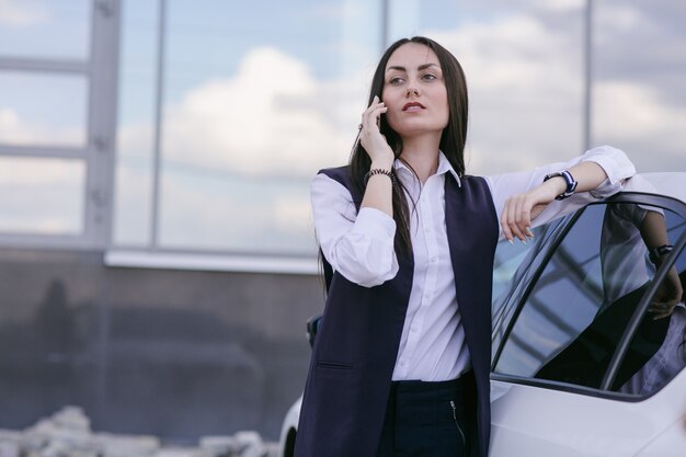 Smiling woman with an elbow leaning on a car while talking on the phone