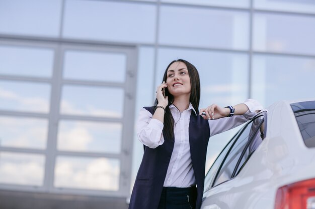 Smiling woman with an elbow leaning on a car while talking on the phone