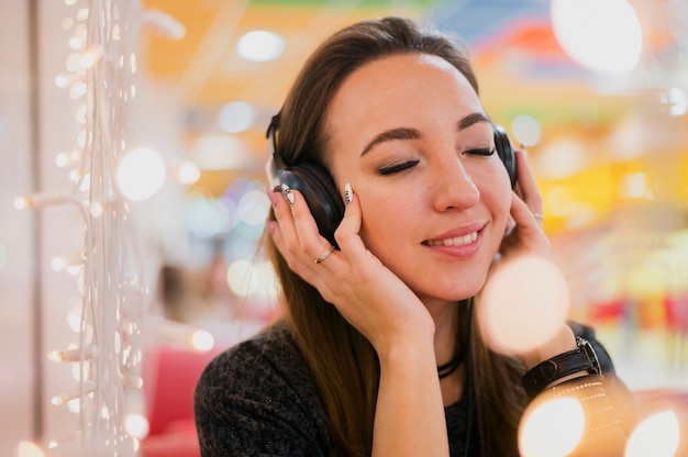 クリスマスライトの近くの頭の上のヘッドフォンを保持目を閉じて笑顔の女性