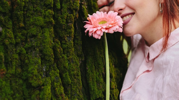 Foto gratuita donna sorridente con il fiore vicino all'albero