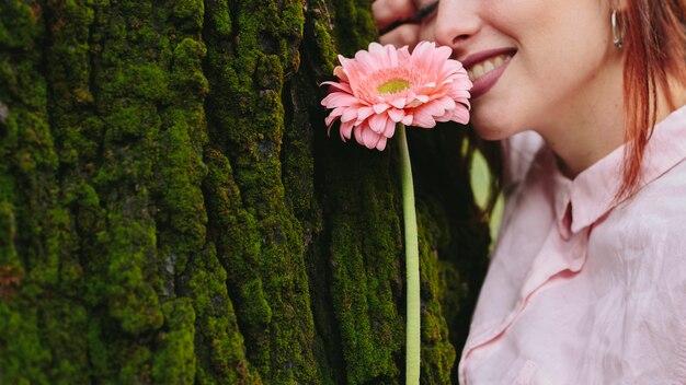 木の近くの花を持つ女性の笑みを浮かべてください。