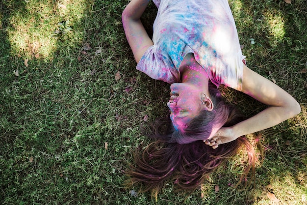 Smiling woman with holi colors lying on green grass