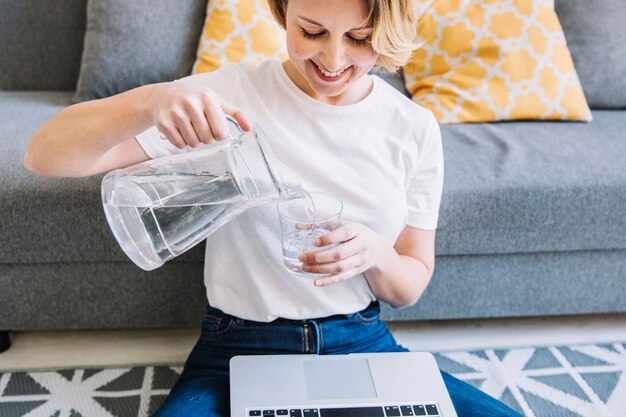 Smiling woman with laptop pouring water