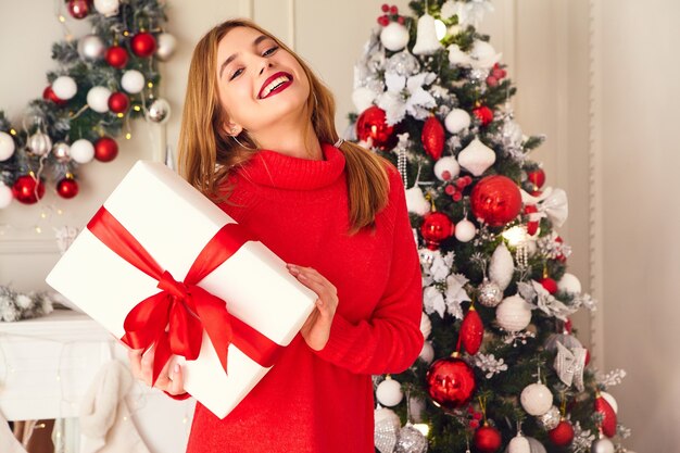 Smiling woman with many gift boxes posing near decorated Christmas tree