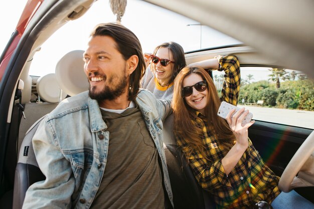 Smiling woman with smartphone and positive man in car near lady leaning out from auto